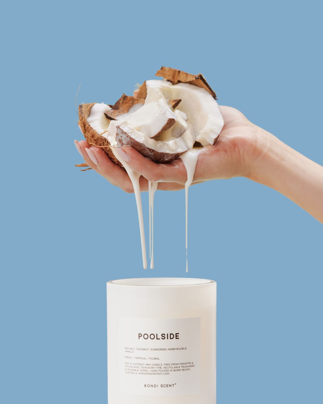 Bondi Scent Poolside coconut scented candle with coconut halves dripping milk held above jar against blue background