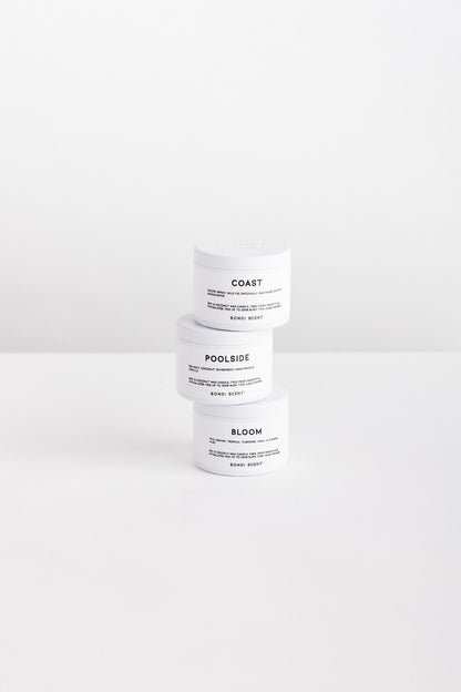 Three white cosmetic jars stacked vertically on a white surface against a white background. The labels read COAST, POOLSIDE, and BLOOM.