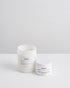 A white glass jar candle called Coast and a white tin candle displayed on a clean white surface against a light gray background.