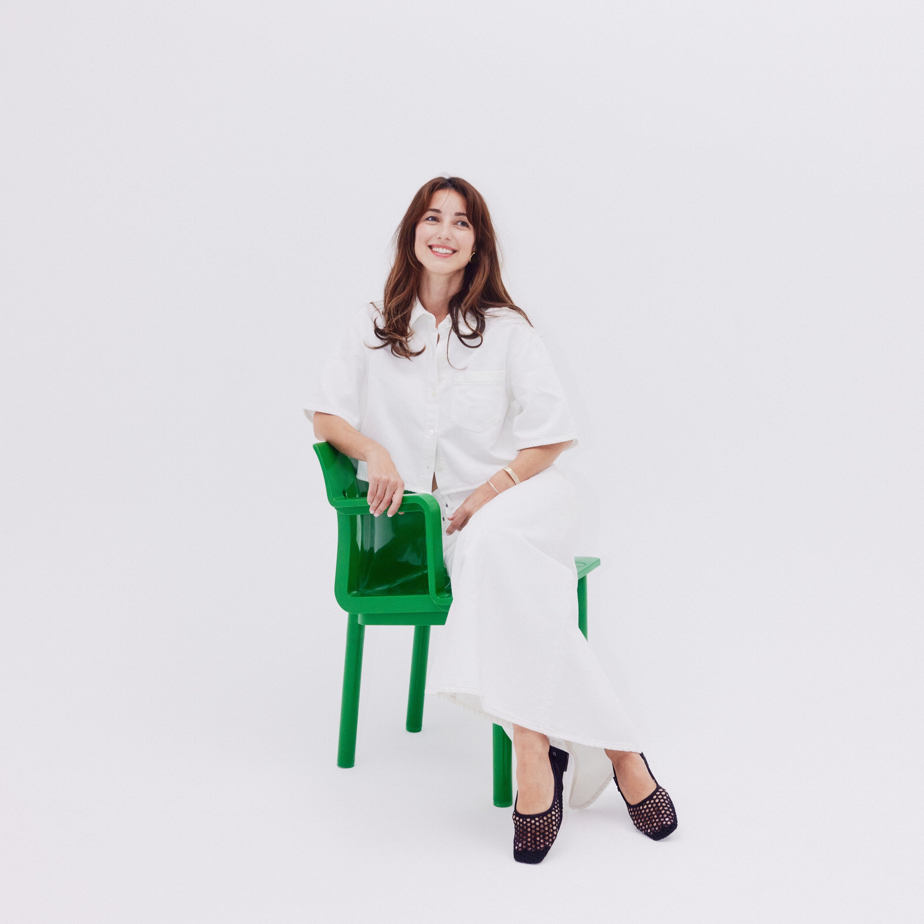 Nina, Founder of Bondi Scent sitting on a green chair against a white background