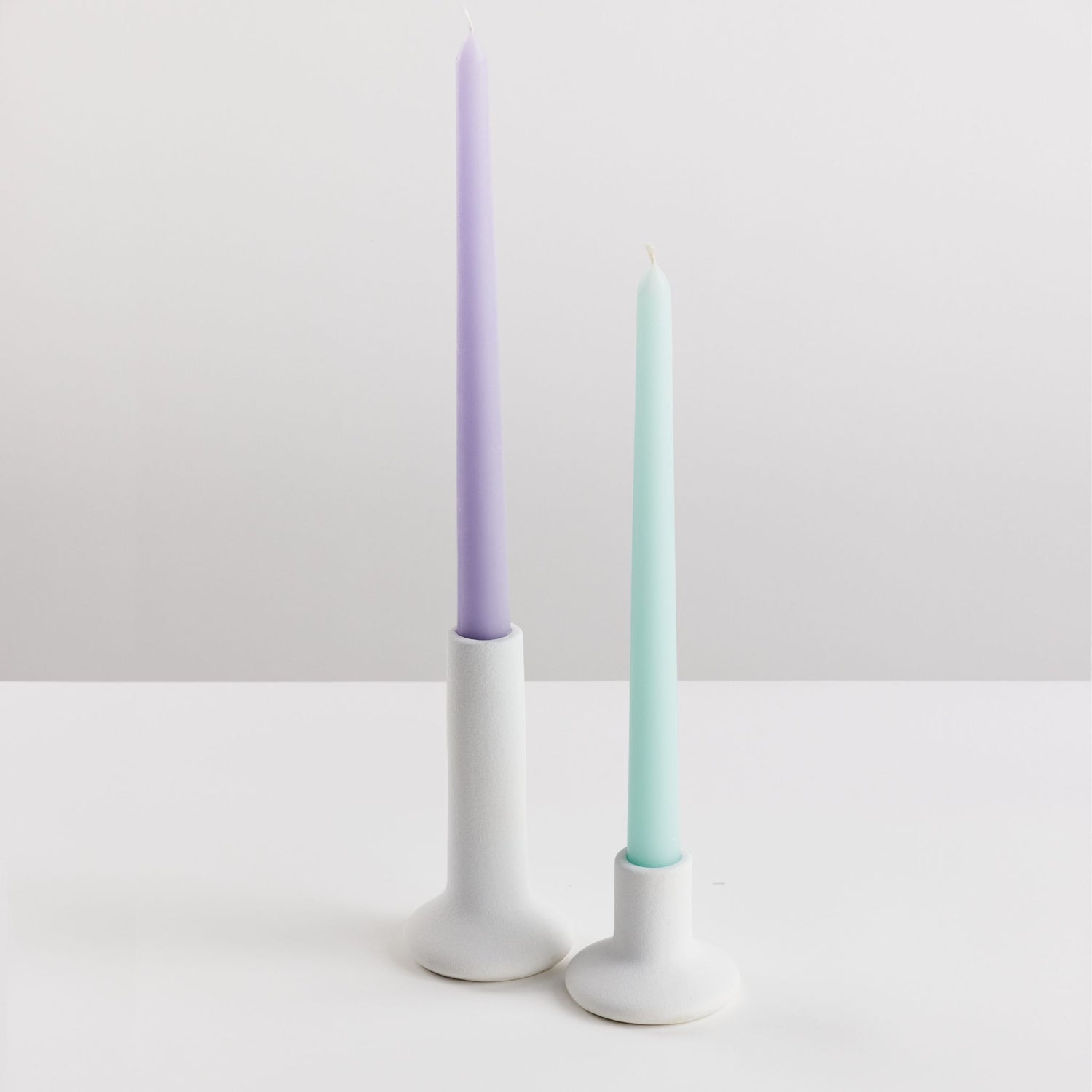 Bondi Scent taper dinner candles in violet and mint with holders on white background