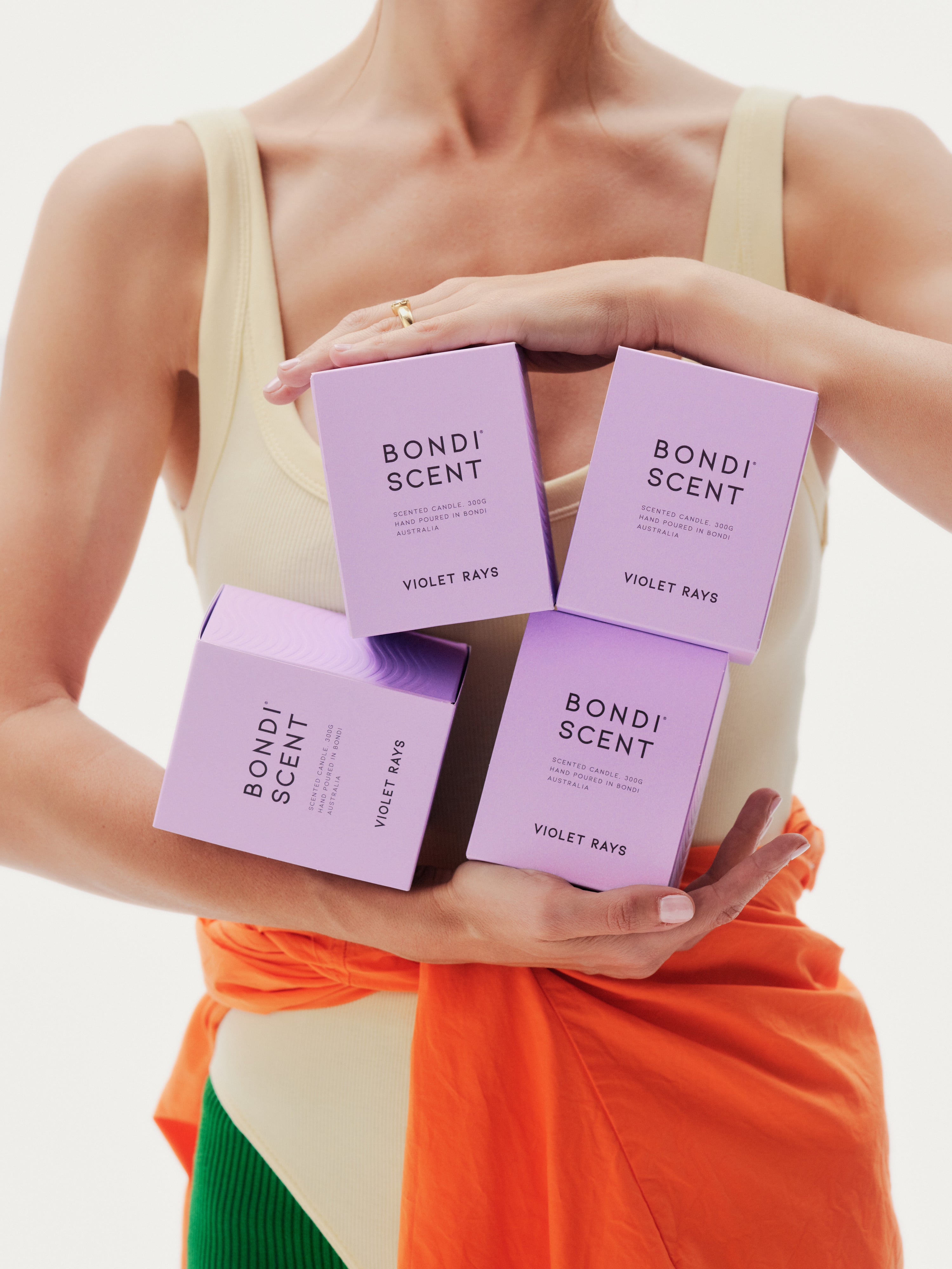 Model holding boxes of 'Bondi Scent Violet Rays' candles against white background